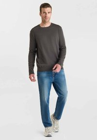 Mörkgrå långärmad skjorta, blå denimjeans och ljusgrå sneakers. Skjortan har rundad hals och ribbat avslut. Avslappnad passform.