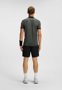 Sportowy strój składający się z dopasowanej, ciemnoszarej koszulki z krótkim rękawem i czarnych szortów, do którego dodano czarną opaskę na nadgarstek oraz białe skarpetki sportowe.