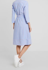 Pasiasta niebieska sukienka z rękawami trzyczwartowymi, z paskiem w talii i kontrastującymi czerwonymi paskami. Miękki materiał o średniej długości dołu i bocznych rozcięciach.