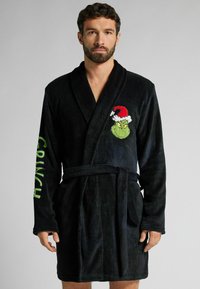 Czarny szlafrok z polaru z haftowanym Grinchem w czapce Miko�łaja na lewej piersi oraz napisem "CRUNCH" w zielonym kolorze na prawej rękawie.