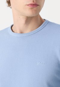 T-shirt a righe di colore blu chiaro con colletto tondo e discreto logo "BOSS" in rilievo sul davanti. Tessuto morbido con una finitura testurizzata.
