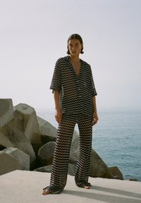 Zwart-wit chevronpatroon set, bestaande uit een losvallend shirt met een V-hals en wijde broekspijpen, gemaakt van lichtgewicht, vloeiende stof.