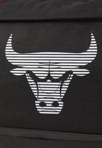 Bolsa de tela negra con un logo de toro de rayas blancas. El diseño presenta contornos distintivos y líneas gruesas que enfatizan las características del toro.