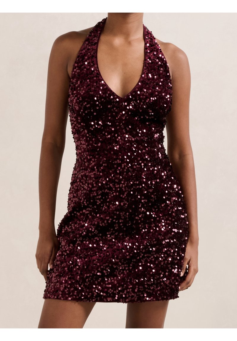 Robe mini sans manches en sequins bordeaux profond avec col halter et décolleté en V portée par une personne debout visible des épaules jusqu'à mi-cuisse.