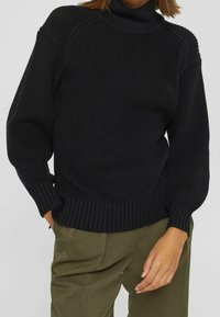 Czarny dziergany golf z prążkowanymi mankietami i dołem. Charakteryzuje się teksturowanym wzorem i luźnym krojem. Połączony z oliwkowymi zielonymi spodniami.