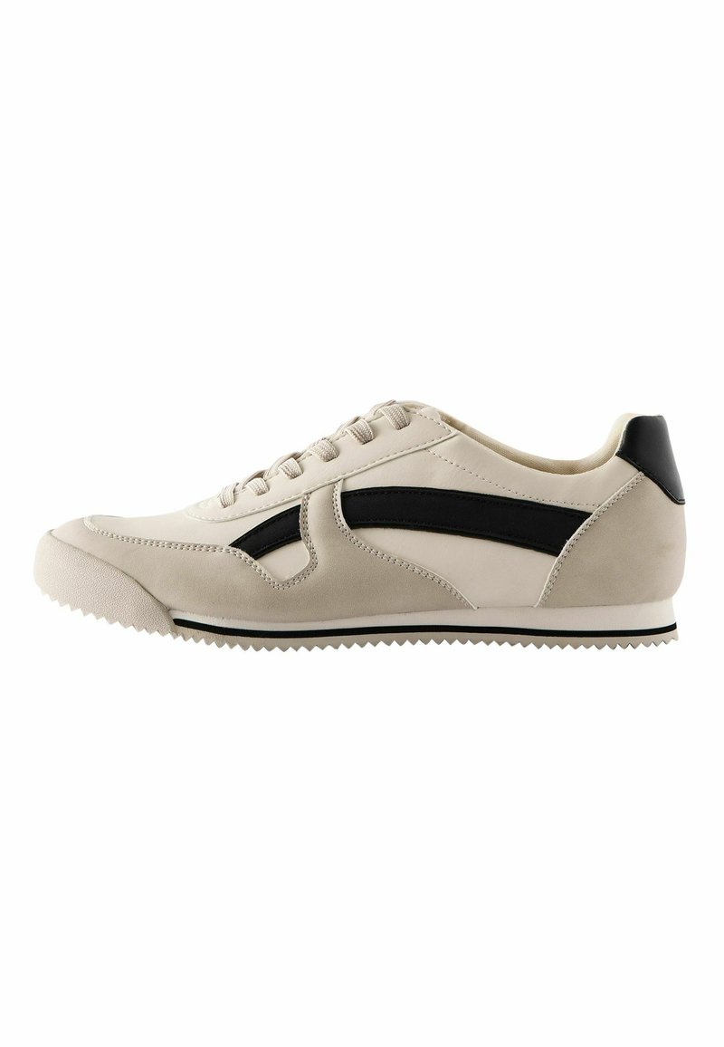 Beige nahka-sneakerit mustilla nahkakoristeilla, joissa on erottuva sivupaneelimuotoilu ja karkea kumipohja pidon parantamiseksi.