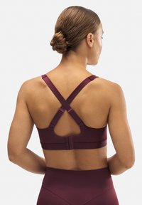 Sujeción deportiva color burdeos con tirantes cruzados, cierre de gancho y textura suave, diseñada para prendas deportivas y comodidad.