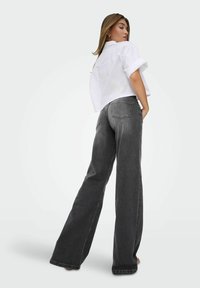 Graue weit geschnittene Jeans und ein weißes, kurzes Button-Up-Shirt mit aufgerollten Ärmeln und Taschenverzierungen, aus einem glatten Stoff gefertigt.