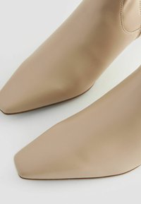 Beige ankle boots with a smooth, matte texture, square toe design, and a sleek silhouette. Minimalistic with no visible hardware or accents.