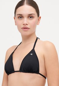Svart bikinitopp med trekantet design, laget av glatt stoff, med justerbare stropper og en liten logo akcent på siden.