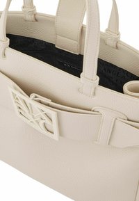 Borsa tote in pelle beige con texture e doppi manici, caratterizzata da una chiusura logo bianca prominente e una fodera interna nera con branding.