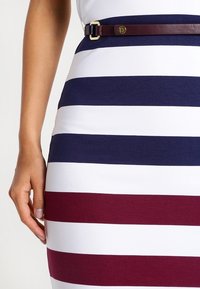 Randig klänning med horisontella blå, vita och burgunderstrimmor; accentuerad med ett tunt, vinrött läderbälte och guldspänne.