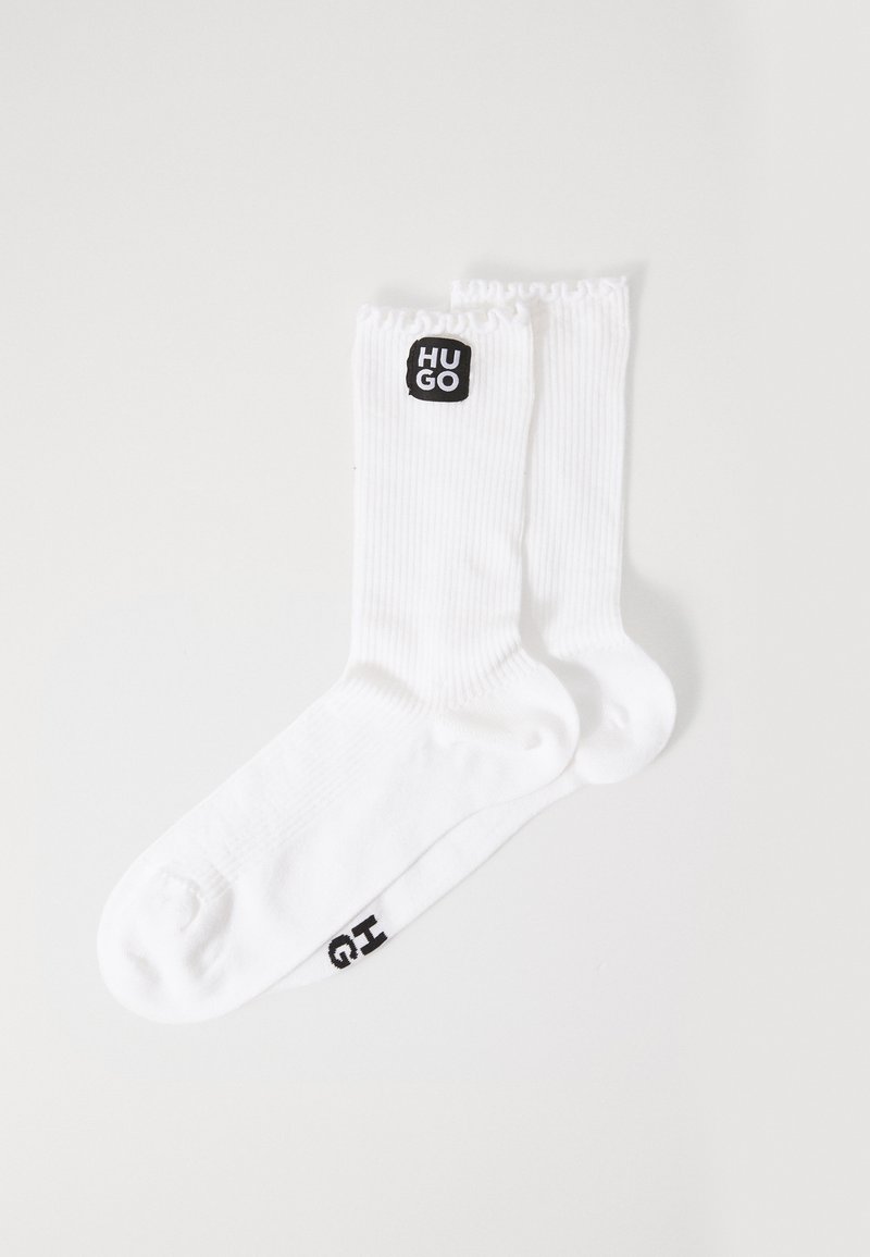 Hvide ribbede sokker med et sort "HUGO" logo-patch på oversiden og et sort "G" detalje på foden. Blød struktur og standardform.