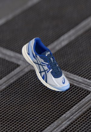 Lightweight athletic shoe in grey and blue, featuring a mesh upper, cushioned sole, and striking side stripes. Rubber outsole with tread detail.