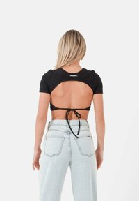 Top nero a maniche corte con apertura sul retro e dettaglio con fiocco, realizzato in tessuto aderente; abbinato a jeans a vita alta con lavaggio chiaro.