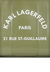 Πράσινο υφασμάτινο υλικό με το "KARL LAGERFELD" τυπωμένο σε λευκό, μαζί με το "ΠΑΡΙΣΙ" και "21 RUE ST-GUILLAUME" σε έντονη γραφή.