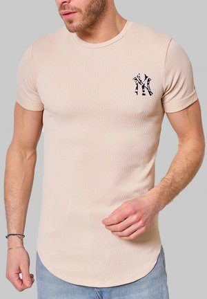 T-shirt en ribbed beige avec des manches courtes, un col rond et un accent logo noir sur la poitrine gauche. La texture semble lisse.
