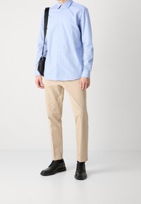 Camicetta azzurre chiaro con bottoni, pantaloni beige su misura e scarpe nere stringate. Vestibilità slim con maniche lunghe e una texture liscia.