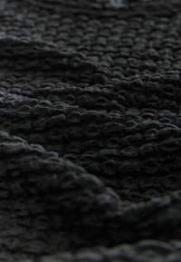 Melna teksturēta auduma ar iešūtu rakstu. Materiāls izskatās mīksts un elastīgs, ar paceltiem laukumiem, kas veido taustāmu virsmu.