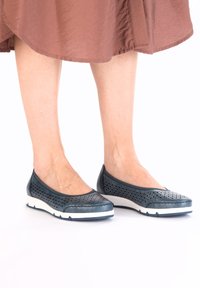 Dark blue perforated flat shoes with a rounded toe and white sole, featuring a textured upper and low profile design.