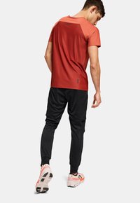 Rød atletisk t-shirt med høj krave, parret med sorte joggingbukser. Skoene er i pink og sort med en tekstureret sål.
