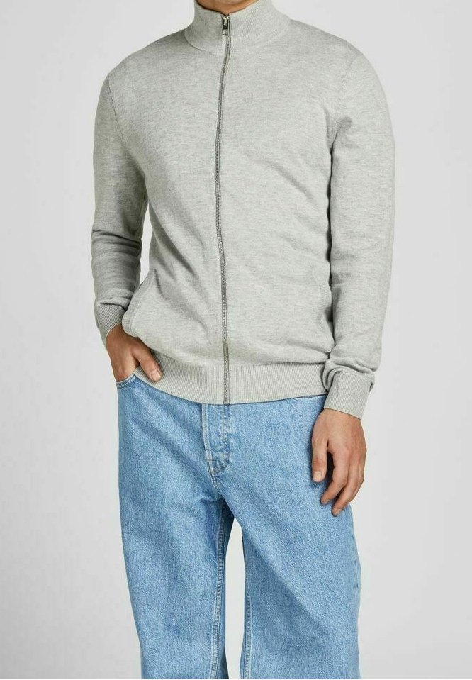 Světle šedá bunda na zip s vysokým límcem, žebrovanými manžetami a spodním lemem, v kombinaci s volnými modrými džínami z denimu. Měkká textura látky.