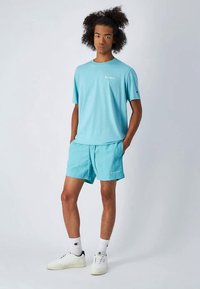 Šviesiai mėlynas marškinėlis ir atitinkamos šortai, pagaminti iš minkštos medžiagos, su maža logo ant krūtinės ir apatinės dalies. Dėvimi su baltais sportbačiais.