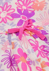 Tissu de robe florale avec des fleurs roses, violettes et orange sur un fond clair, avec un lien en ruban rose à la taille. La texture est légère.