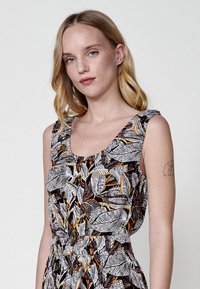 Ärmelloses Kleid mit rundem Ausschnitt und gerafftem Detail an der Taille. Es hat ein tropisches Blättermuster in Schwarz, Weiß und Orange.