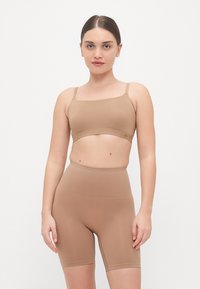 Bešavna, rebrasta, svijetlosmeđa bralette s tankim trakama i visokim šorcima u odgovarajućoj boji, izrađeni od rastezljivog, glatkog materijala.
