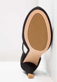 Mustat mokkanahka korkokengät, joissa on mantelinmuotoinen kärki, vaaleanruskea kumipohja, jossa on teksturoitu pito, sekä avonainen takaosa.