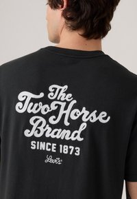 Černé bavlněné tričko s bílým vyšitým textem: "The Two Horse Brand," "Since 1873," a "Levi's" na zadní straně.