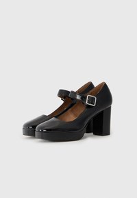 Black patent leather Mary Jane shoes with a round toe, adjustable strap, and chunky block heel. Smooth texture with a shiny finish.