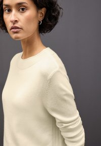 Maglione chiaro di crema con scollo rotondo, dettagli a costine sulle spalle e particolari testurizzati ai lati. Realizzato in morbido tessuto lavorato a maglia.