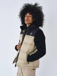 Gilet imbottito beige con maniche nere, chiusura con zip frontale e tasche laterali. Presenta un piccolo logo sul petto e una texture del tessuto liscia.