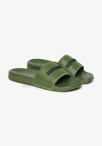 Groene slidingssandalen met een brede band met zwart "SUPERDRY" logo. Gemaakt van glad materiaal met een gevoerde zool. Plat ontwerp.