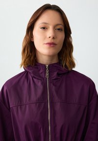 Paarse hooded jack met een ritssluiting aan de voorkant en subtiele glans. Gladde textuur, relaxed fit, en geen zichtbare patronen of versieringen.