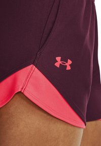 Vínové sportovní kraťasy s růžovým spodním lemem, s logem Under Armour na boku, vyrobené z pružného elastického materiálu.