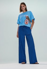 T-shirt bleu oversize avec détail et motif léopard. Pantalon large à jambes larges à carreaux bleu clair. Coupe décontractée, manches courtes et taille à cordon de serrage.