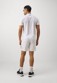Polo deportivo blanco de manga corta, combinado con pantalones cortos blancos con rayas negras, llevados con zapatillas negras y calcetines blancos.