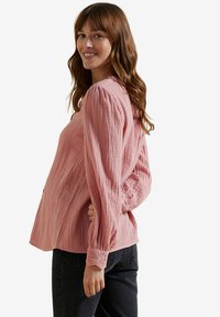 Rosa strukturierte Bluse mit langen, puffigen Ärmeln und Lochmuster an den Bündchen, kombiniert mit schwarzen Jeans. Einfaches und lässiges Design.
