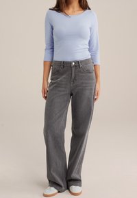 Ljusblå långärmad topp i kombination med grå vida jeans. Jeansen har knappstängning och framfickor; mjukt, strukturerat tyg.