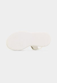 Semelle de sandale blanche avec des rainures horizontales et une marque de taille 38, vue par le dessous sur un fond blanc uni.