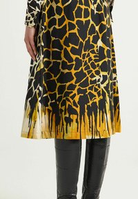 Abito in tessuto con motivo a giraffa in giallo e nero con finitura lucida. Caratterizzato da un design svasato e orlo dettagliato. Indossato con leggings neri a trama.