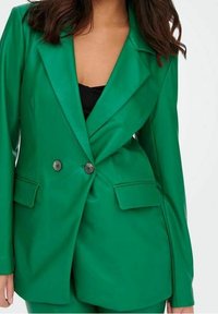 Blazer verde realizzato in un tessuto liscio, con un davanti doppiopetto con bottoni neri, rever a punta e tasche laterali.