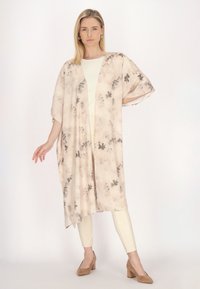 Lette, gennemsigtige kimono i beige med grå blomsterprint. Åben front, korte ærmer og afslappet pasform. Sammen med lyse leggings og brune hæle.