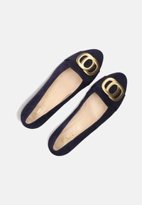 Navyblauwe suède platte schoenen met een grote gouden dubbele gesp en een gladde beige binnenzool met de merknaam "Gabor" in gouden letters.