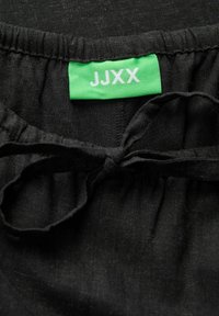 Tissu noir avec une taille élastique froncée et un détail à nouer. Présente une étiquette verte avec un texte blanc indiquant "JJXX."