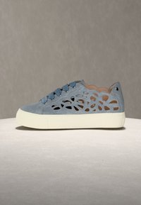 Ανοιχτό μπλε αθλητικό παπούτσι με λουλουδάτα κοψίματα, παχύ λευκό πέλμα, μπλε κορδόνια και στρογγυλεμένη μύτη, επάνω σε ουδέτερη επιφάνεια και φόντο.