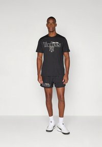 Crna pamučna majica i set kratkih hlača s logotipom "New York Yankees" u bijeloj i zlatnoj boji. Okrugli izrez, kratki rukavi i opušteni kroj.